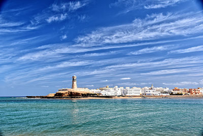 Lighthouse by sea against buildings in city