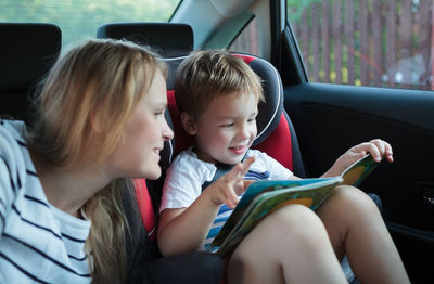 Mother and son reading book while sitting in car