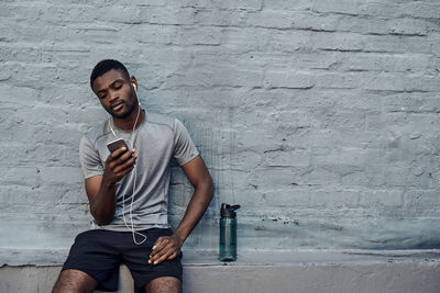 Young man sitting against wall