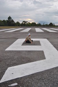 Woman sitting on runway against cloudy sky