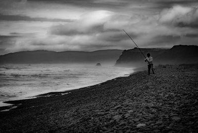 Man fishing on beach against sky