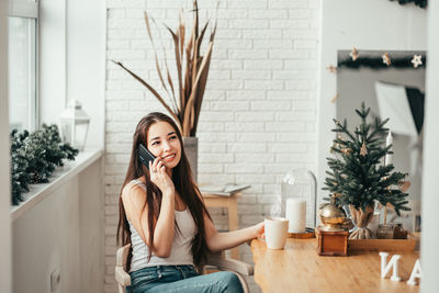 Young woman using smart phone while sitting on laptop