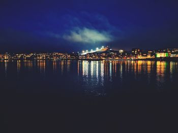 Illuminated city by sea against sky at night