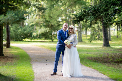 Full length portrait of bride and bridegroom standing on footpath at park