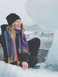 Portrait of smiling young woman standing at beach during winter