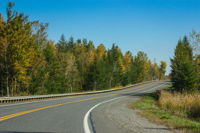 Empty road amidst trees against clear sky