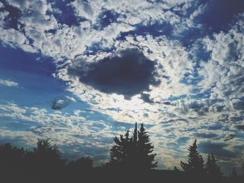 Low angle view of trees against cloudy sky