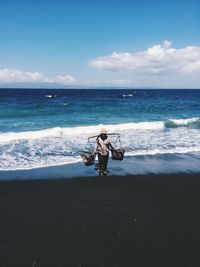 Full length of vendor with baskets at beach against sky