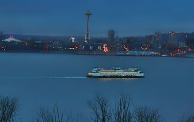 Illuminated city by river against sky at dusk