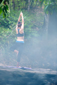 Rear view of teenage girl practicing tree pose in forest