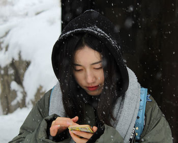 Close-up of young woman using phone during snowfall