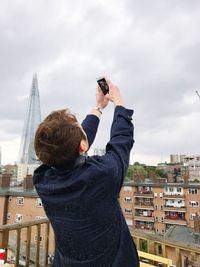 Rear view of man photographing against sky in city