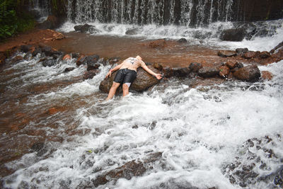 Full length of boy splashing water in waterfall