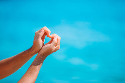 Cropped hands of man making heart shape against sea