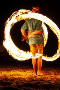 Midsection of man standing against illuminated fire at night