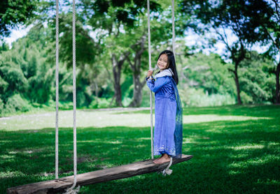 Full length of cute girl standing on rope swing at park