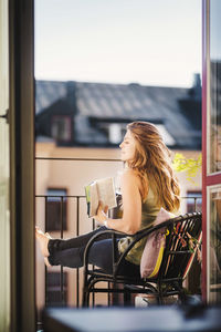 Side view of woman looking away while holding guidebook at balcony