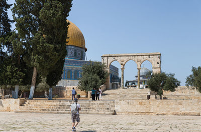 People walking in front of historical building against clear sky