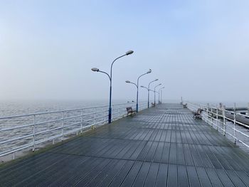 Street lights on footpath by sea against clear sky