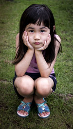 Portrait of cute girl crouching on field with hands on chin