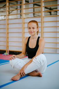 Smiling female athlete sitting on floor in gym