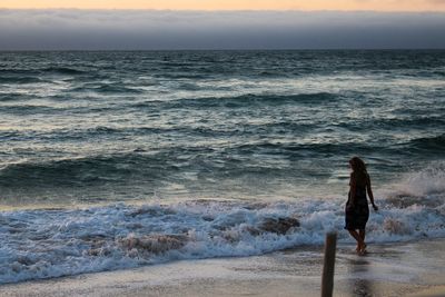 Woman walking on beach against sky during sunset