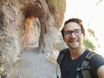 Portrait of smiling young man standing against arch in rock formation