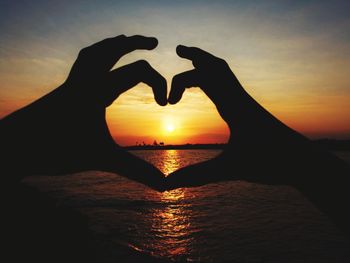 Silhouette hand holding heart shape against sky during sunset