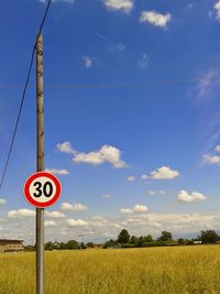Road sign on pole by field against sky