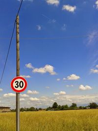 Road sign on field against sky