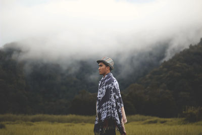 Portrait of young man standing in grass against sky