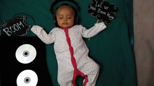 Cute baby girl wearing headphones while lying on bed 