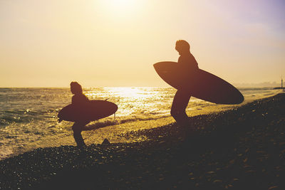 Rear view of silhouette people on beach against sky during sunset