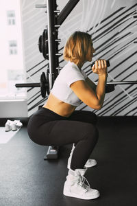 A sporty girl performs squats with dumbbells during a workout in the gym.