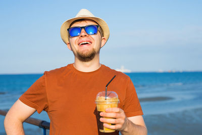 Young man drinking water from glass against sea