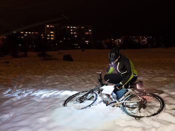 Man riding bicycle on snow in city at night