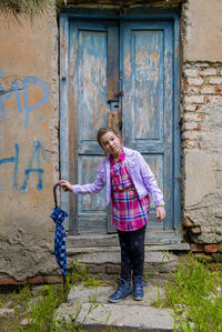 Portrait of girl holding umbrella while standing by old closed door