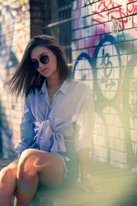 Portrait of young woman sitting on seat against graffiti wall