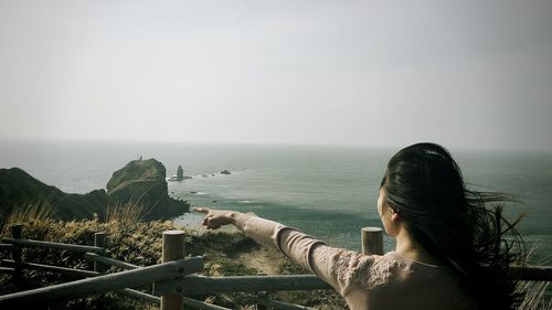 Rear view of woman standing by sea against clear sky