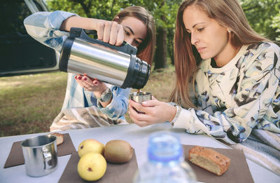 Woman pouring tea in cup held by friend at camp