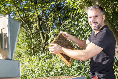 Portrait of man holding honeycombs against trees