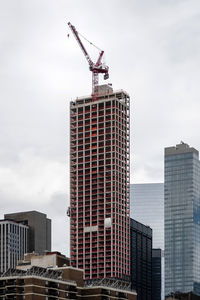 Low angle view of crane by buildings against sky