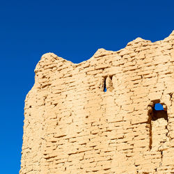 Low angle view of stone wall against clear blue sky