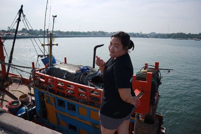 Portrait of smiling woman standing against fishing boat on sea