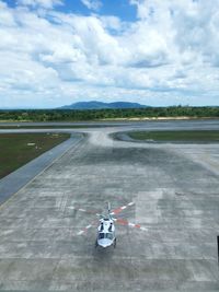 High angle view of helicopter at airport runway against cloudy sky
