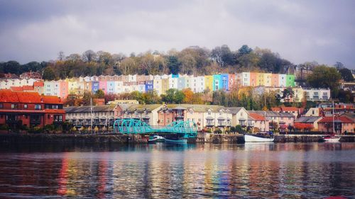 Buildings by river against sky in city