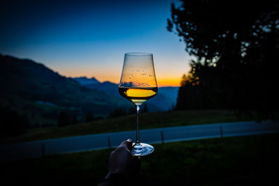 Person holding drink against sky during sunset