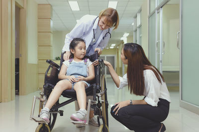 While the doctor comes to see her, a young asian girl patient smiles in her wheelchair.