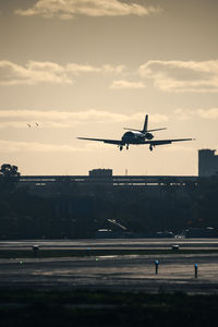 Airplane flying over airport runway against sky