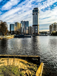 Modern buildings by river against sky in city